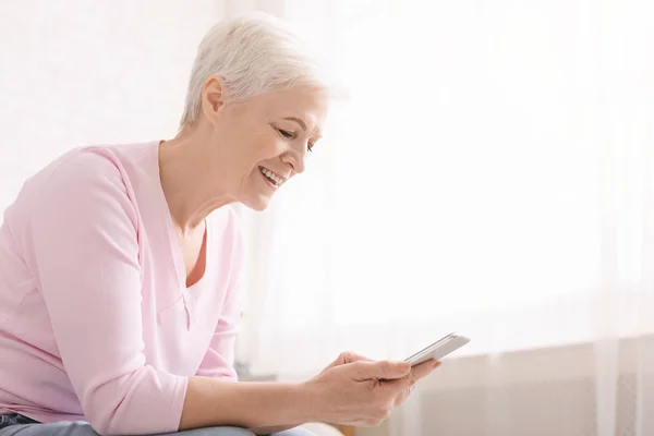 Positive Rentnerin nutzt modernes Smartphone zu Hause — Stockfoto
