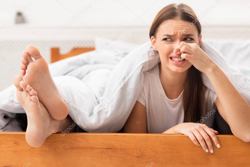 Girlfriend Pinching Nose Lying Near Boyfriends Smelly Feet In Bed