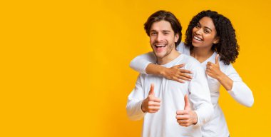 Olumlu çok ırklı çift sarılıp başparmaklarını göstererek bir şeyler öneriyorlar.