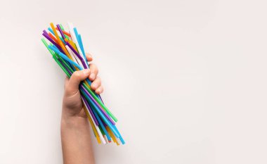 Hand holding heap of used plastic straws on white
