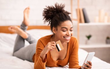 Happy Woman Using Smartphone And Credit Card Lying In Bed