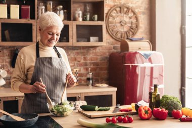 Senior lady cooking fresh salad at home kitchen