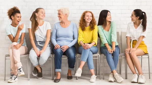 Mulheres alegres e diversas conversando sentadas em cadeiras internas, Panorama — Fotografia de Stock
