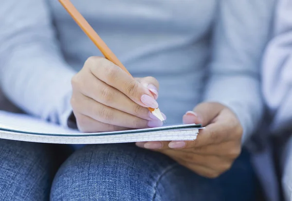 Обрізана студентка бере нотатки, використовуючи блокнот і олівець — стокове фото