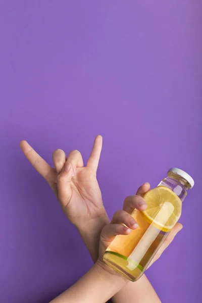 Frau zeigt Horn-Zeichen und hält Flasche mit köstlichem Zitronen-Entgiftungswasser — Stockfoto