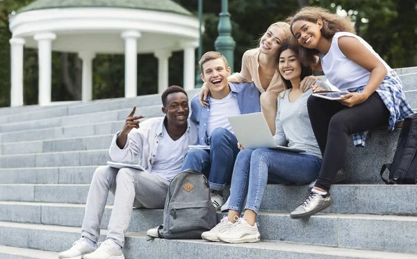 Szczęśliwi studenci uśmiechnięci do kamery podczas odrabiania lekcji na świeżym powietrzu — Zdjęcie stockowe