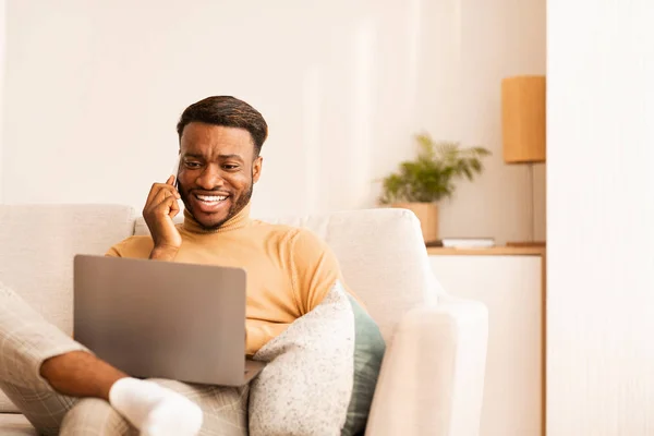 Guy Working On Laptop Chatting On Phone Sitting At Home