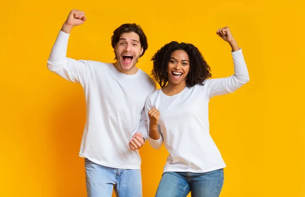 Overjoyed interracial couple celebrating success with raised fists over yellow background — Stockfoto