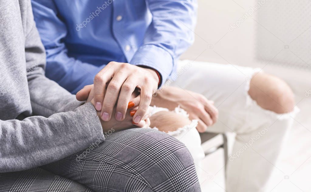 Closeup of unrecognizable man comforting his wife, holding her hands