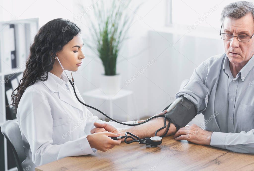Female doctor checking blood pressure of mature man