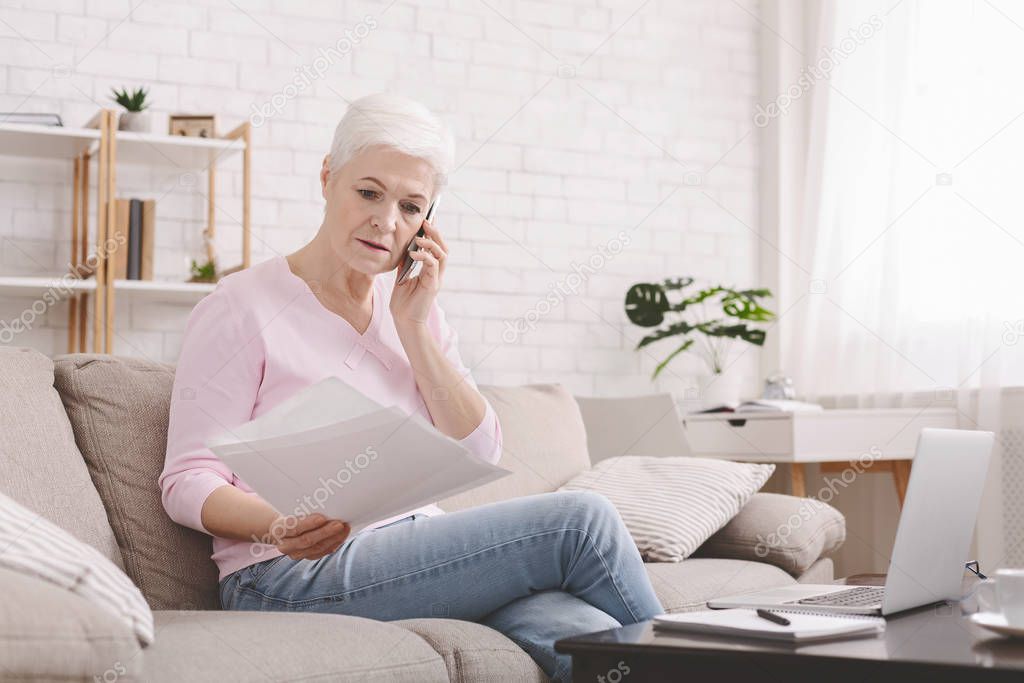 Senior lady reading document and talking to advisor by phone