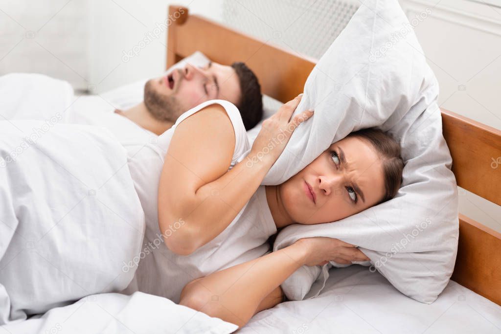 Angry Girlfriend Covering Ears Lying Near Snoring Boyfriend In Bed