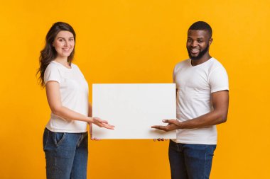 Young woman and afro man holding and pointing at blank placard