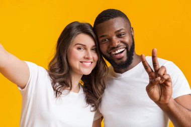 Mutlu, interrasyonel bir çift selfie çekiyor, kameraya bakıyor ve gülümsüyor.