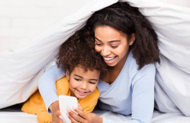 Mutlu Siyah Anne ve Kızı Yatakta Uzanmış Akıllı Telefonu Kullanıyor