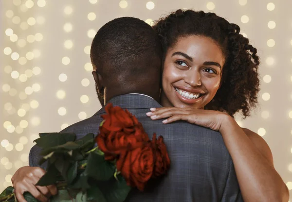 Χαμογελώντας άφρο γυναίκα κρατώντας κόκκινα τριαντάφυλλα, ενώ αγκαλιάζει τον άντρα της — Φωτογραφία Αρχείου