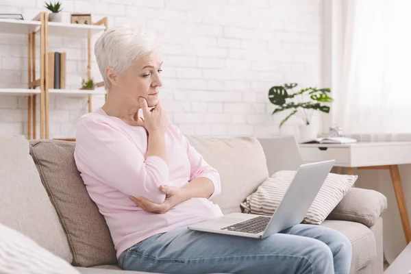 Μπερδεμένη ηλικιωμένη κυρία κοιτάζοντας το laptop με αμηχανία — Φωτογραφία Αρχείου