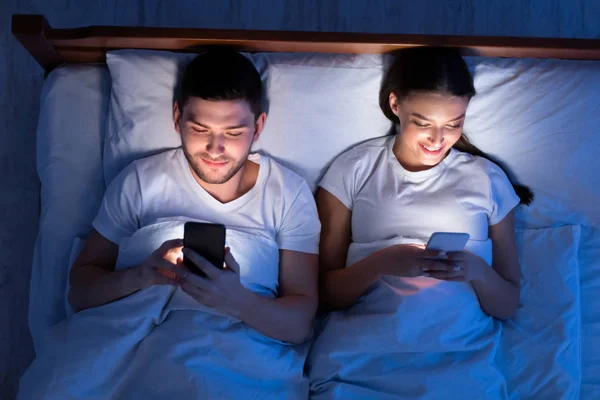 Casal usando smartphones deitados na cama em casa, vista superior — Fotografia de Stock