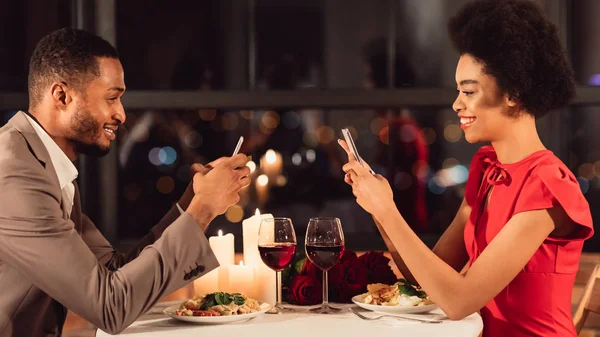 Afro Ζευγάρι Χρησιμοποιώντας Smartphones Κατά τη διάρκεια ρομαντική ημερομηνία στο εστιατόριο, Πανόραμα — Φωτογραφία Αρχείου