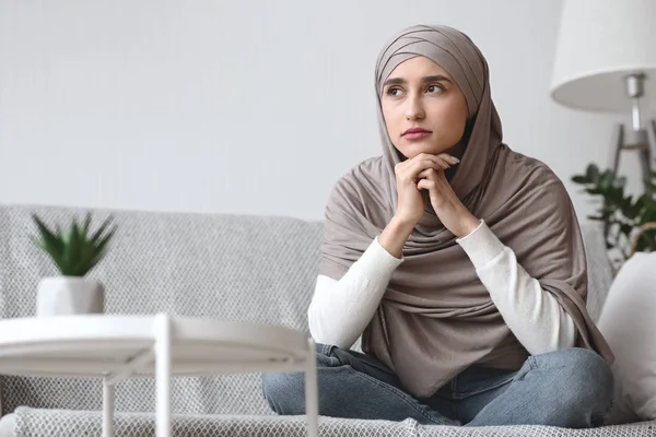 Zamyšlená nešťastná arabská žena v hidžábu sedí doma na gauči — Stock fotografie