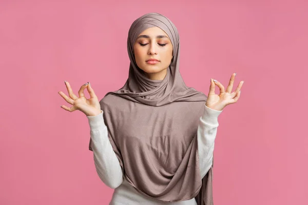 Gadis muslim yang santai bermeditasi di atas latar belakang merah muda — Stok Foto