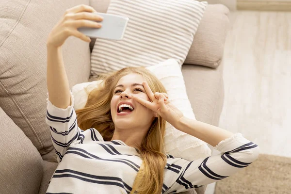Chica feliz tomando selfie mientras está acostado en el sofá — Foto de Stock