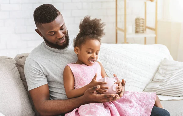 Genç afro baba küçük kızına kumbarayı gösteriyor. — Stok fotoğraf