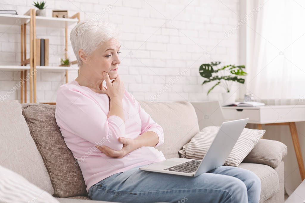 Puzzled senior lady looking at laptop with perplexity