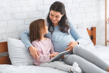 Güzel, hamile bir kadın ve dijital tablet kullanan küçük tatlı bir kız.