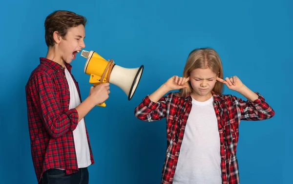 Маленькая девочка закрывает уши, в то время как ее старший брат кричит мегафон — стоковое фото