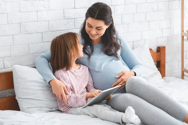 Schöne schwangere Frau und süße kleine Tochter mit digitalem Tablet — Stockfoto
