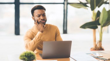 Ofiste dizüstü bilgisayarla çalışan odaklanmış siyah bir adam.