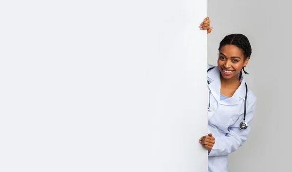 Junge Ärztin blickt aus weißer Werbetafel — Stockfoto