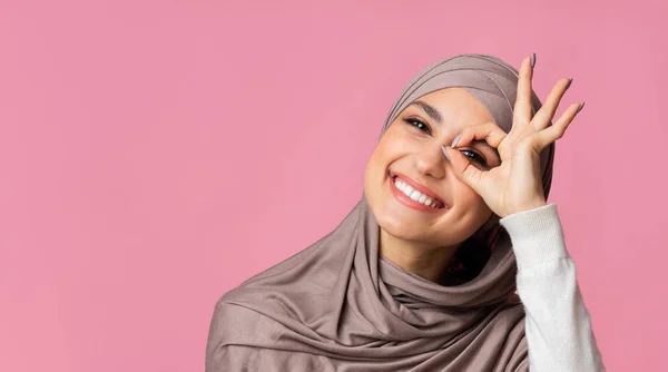 Glückliches arabisches Mädchen mit Kopftuch blickt durch o.k. Geste in die Kamera — Stockfoto