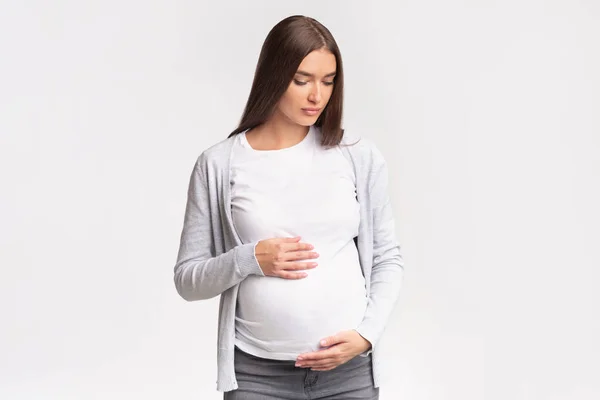 Έγκυος γυναίκα κοιτάζει κάτω αγγίζοντας την κοιλιά ποζάροντας στο στούντιο — Φωτογραφία Αρχείου