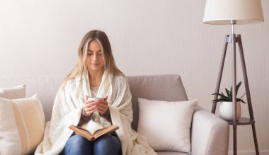 Hayalperest kız kitap okuyor ve evde sıcak kahvenin tadını çıkarıyor.