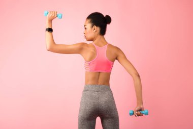 Pembe Arkaplan ve Arka Görüş Üzerinde Dambıllarla Egzersiz Yapan Afrikalı Amerikalı Kadın