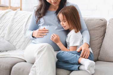 Anaokulu kızı annesinin karnına sarılıyor.