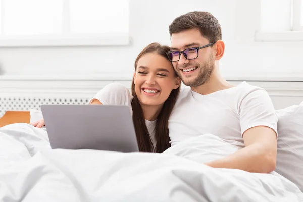 Ζευγάρι βλέποντας ταινία στο φορητό υπολογιστή κάθεται στο κρεβάτι στο σπίτι — Φωτογραφία Αρχείου