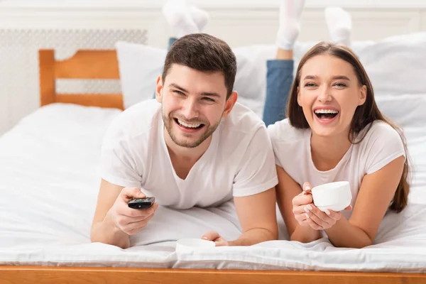 Casal alegre assistindo TV relaxante deitado na cama de manhã — Fotografia de Stock