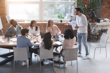 Genç iş adamları toplantı yapıyor, pazarlama raporlarını dinliyor.
