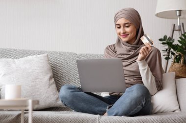 Başörtülü, laptoplu ve kredi kartlı Müslüman bir kadın.