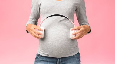 Müzik ve hamilelik. Karnının yanında kulaklık tutan bir kadın bekliyor.