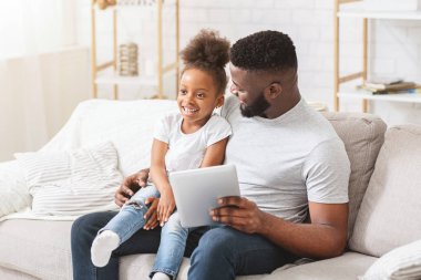 Siyah baba ve kızı evde dijital tablet kullanıyorlar.