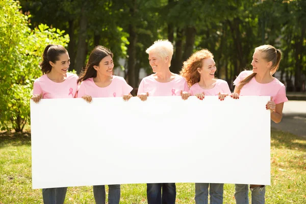 Señoras de rosa camisetas sosteniendo cartel en blanco de pie en el parque — Foto de Stock