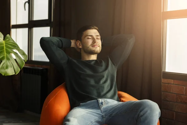Slappet av på Millennial Guy Sitting on Beanbag Chair in Modern Interior – stockfoto