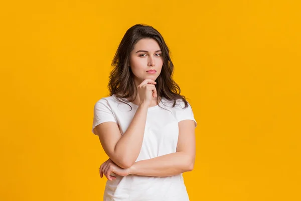 Skeptische junge Frau berührt Kinn und blickt misstrauisch in die Kamera — Stockfoto