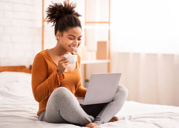 Afričanky americká dívka pomocí notebooku s kávou sedí v posteli — Stock fotografie