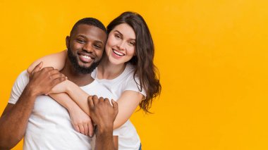 Sarı arka planda birlikte poz veren mutlu çok ırklı çiftin portresi.