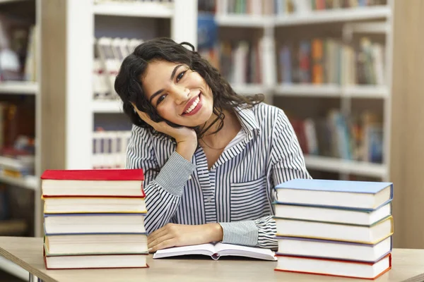 Sorrindo latina menina sentada na mesa na biblioteca — Fotografia de Stock